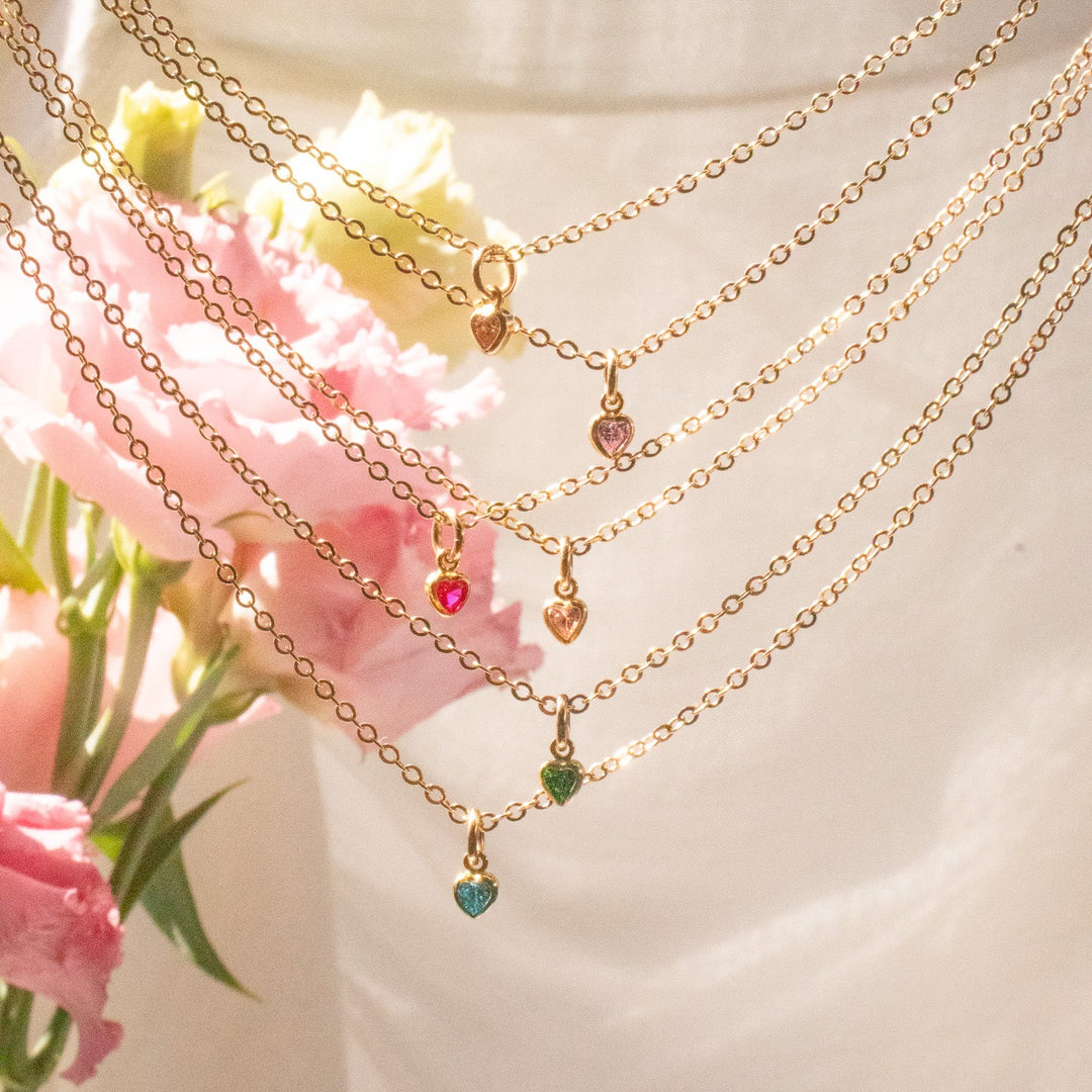 Gold necklaces with colorful pendants on a mannequin against a floral background