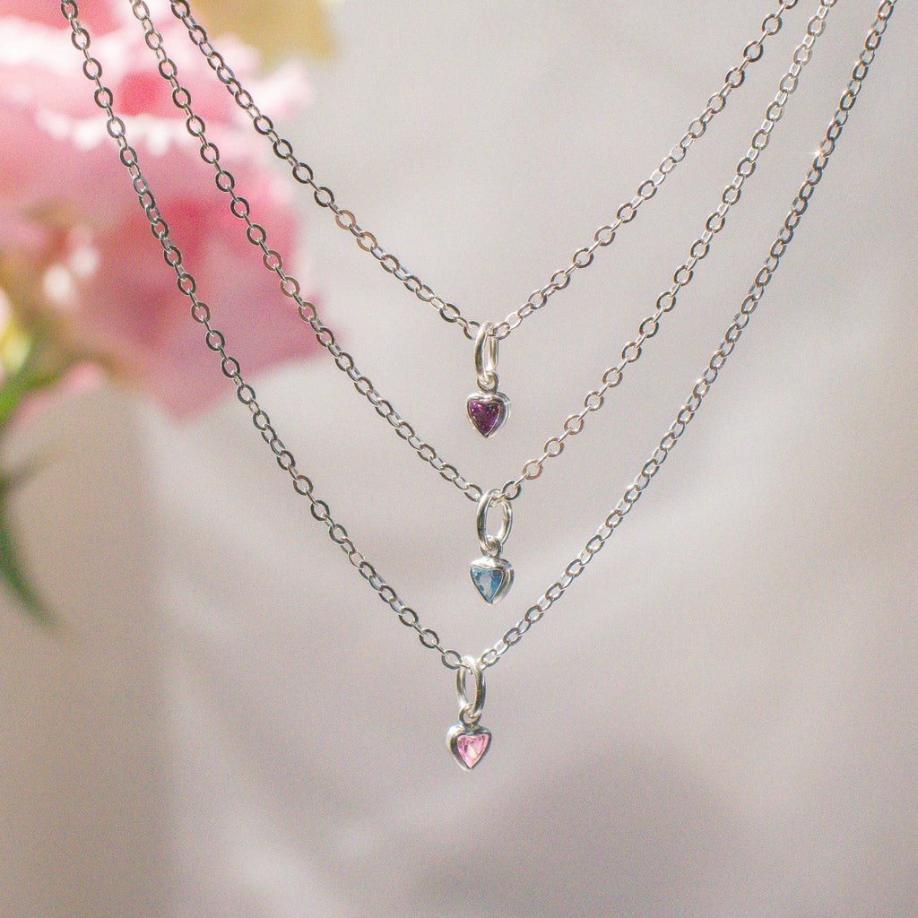 Two silver necklaces with heart-shaped pendants on a blurred floral background