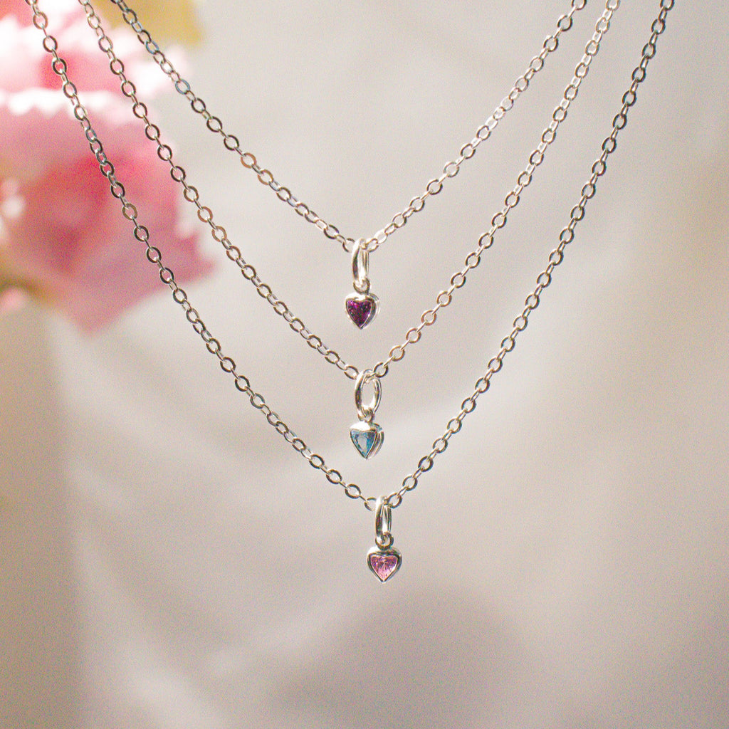 Three delicate necklaces with heart-shaped charms on a soft background