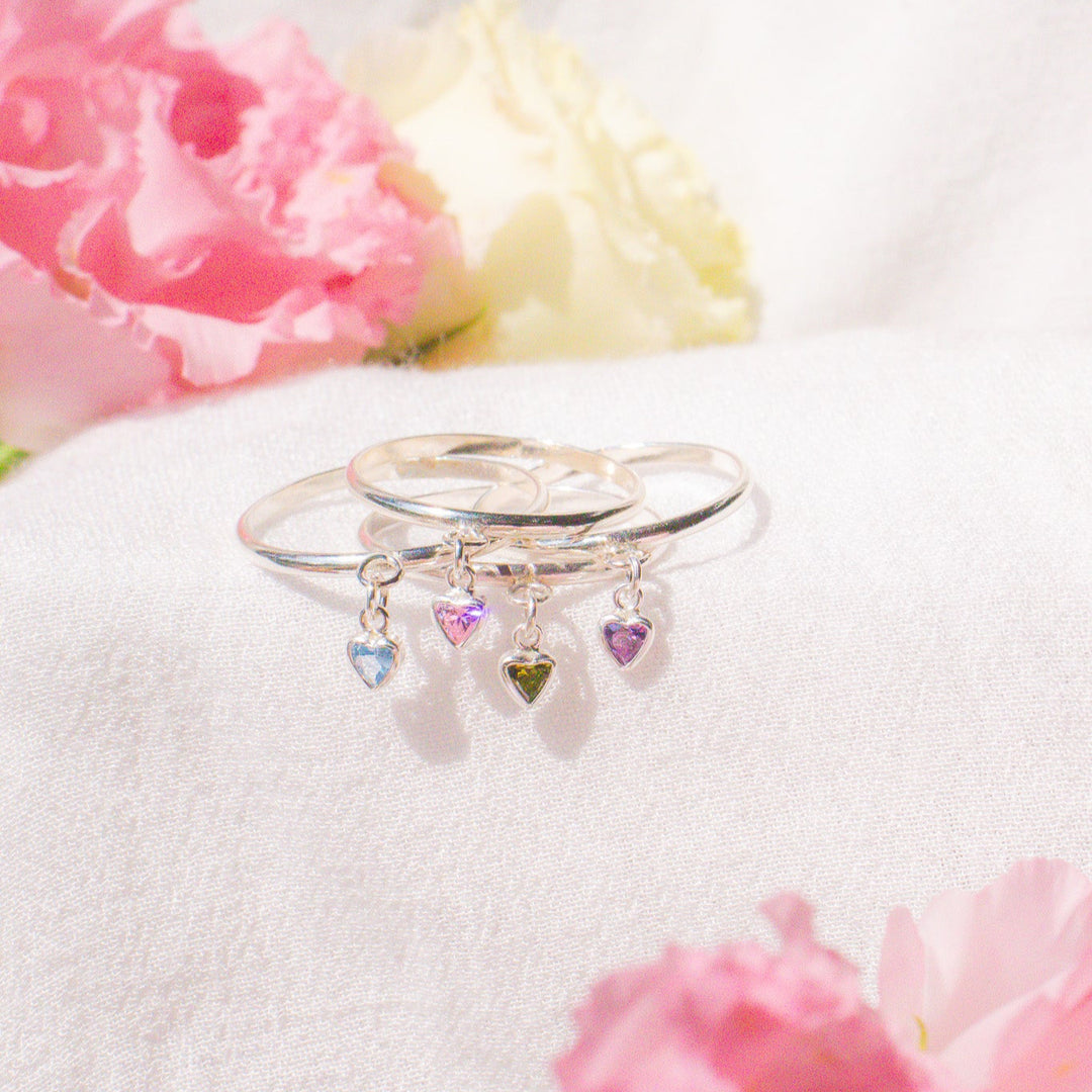 Silver ring with heart-shaped charms on a white surface with pink flowers