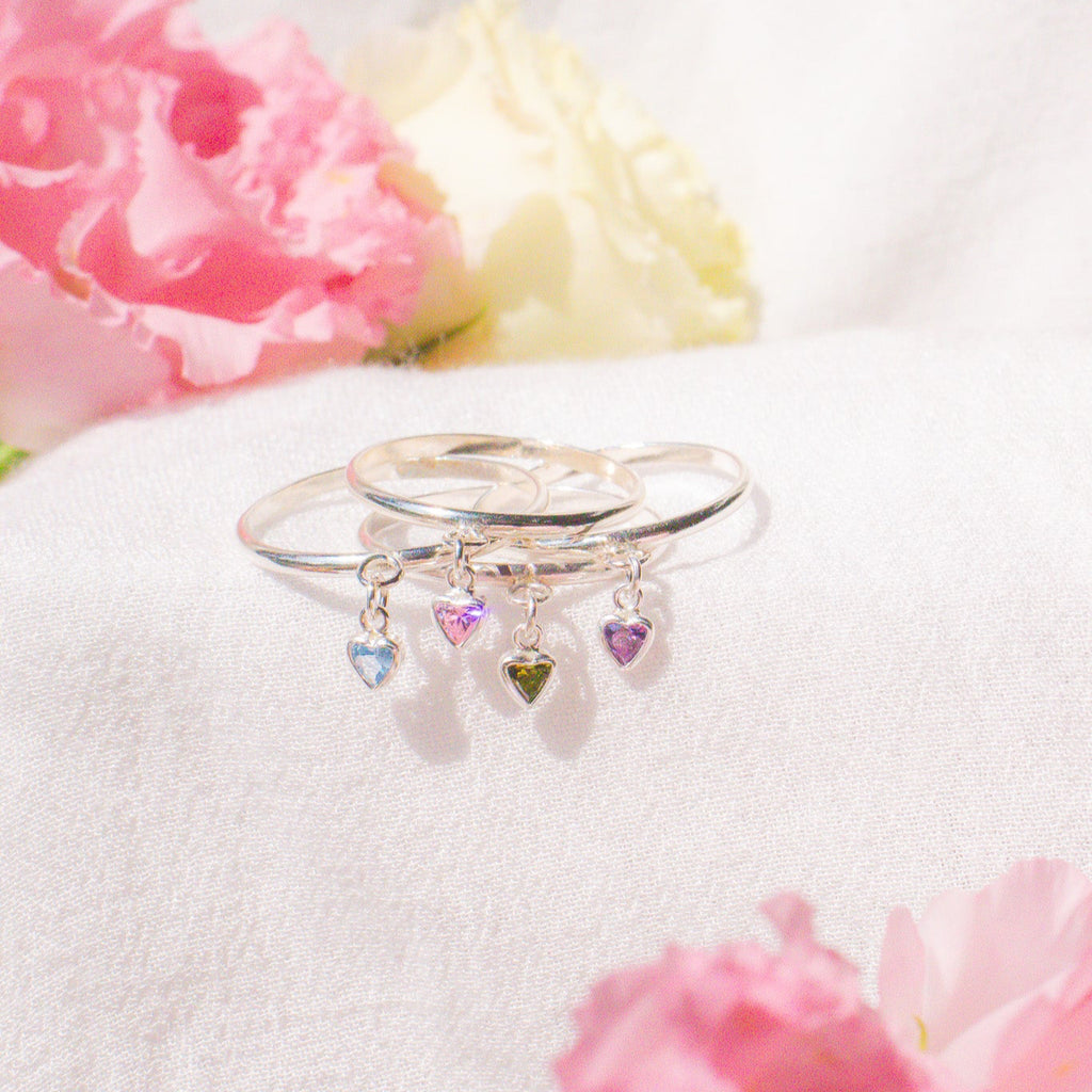 Silver ring with heart-shaped charms on a white surface with pink flowers