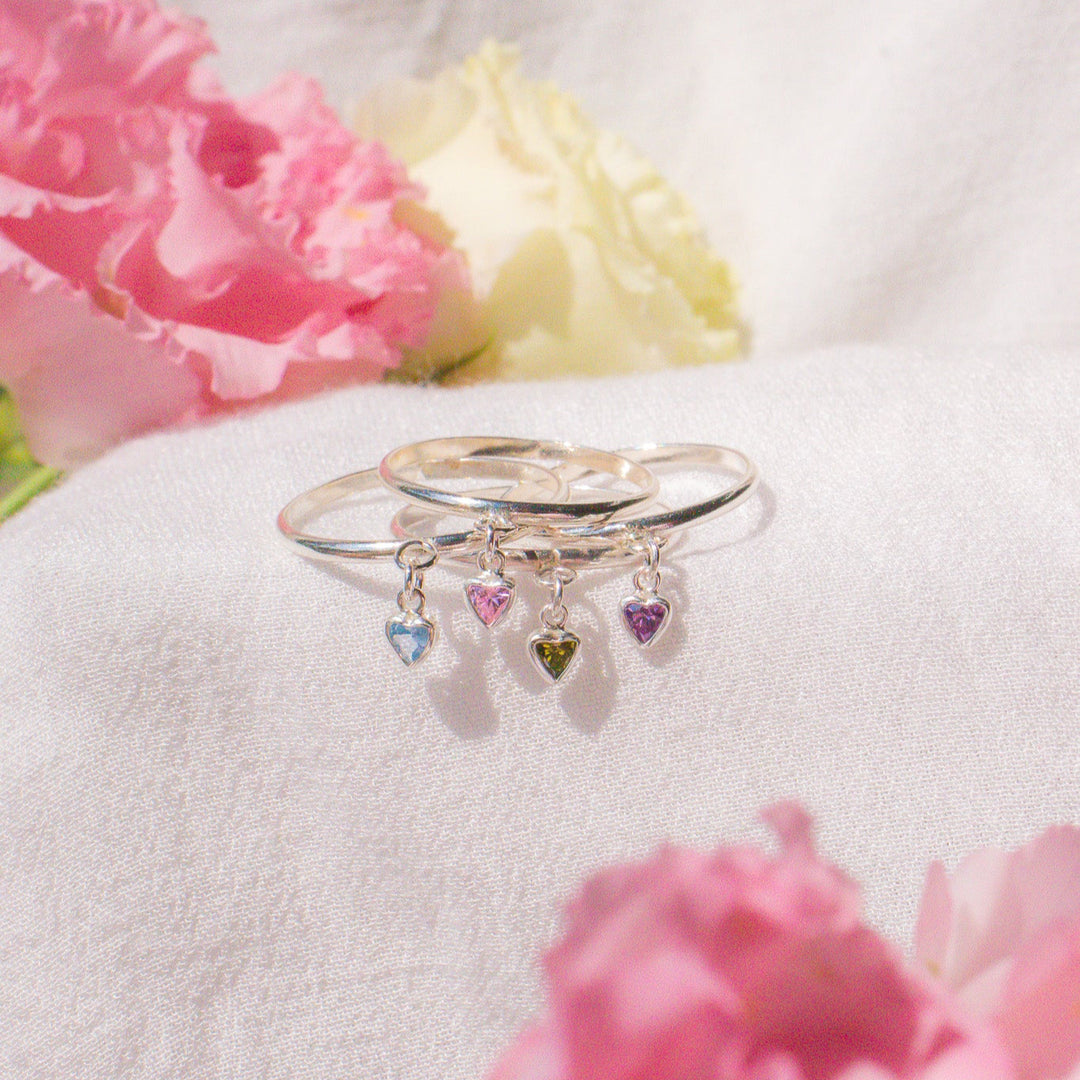 Silver ring with colorful heart-shaped charms on a white surface with pink flowers.