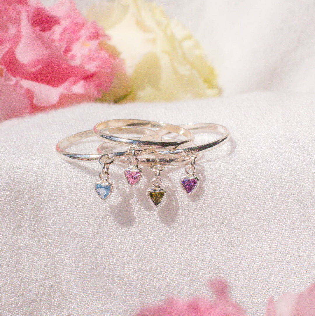Silver ring with heart-shaped charms on a white surface with pink flowers