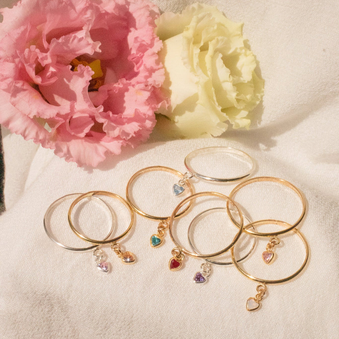 Gold and silver rings with charms on a light fabric background with pink and white flowers.