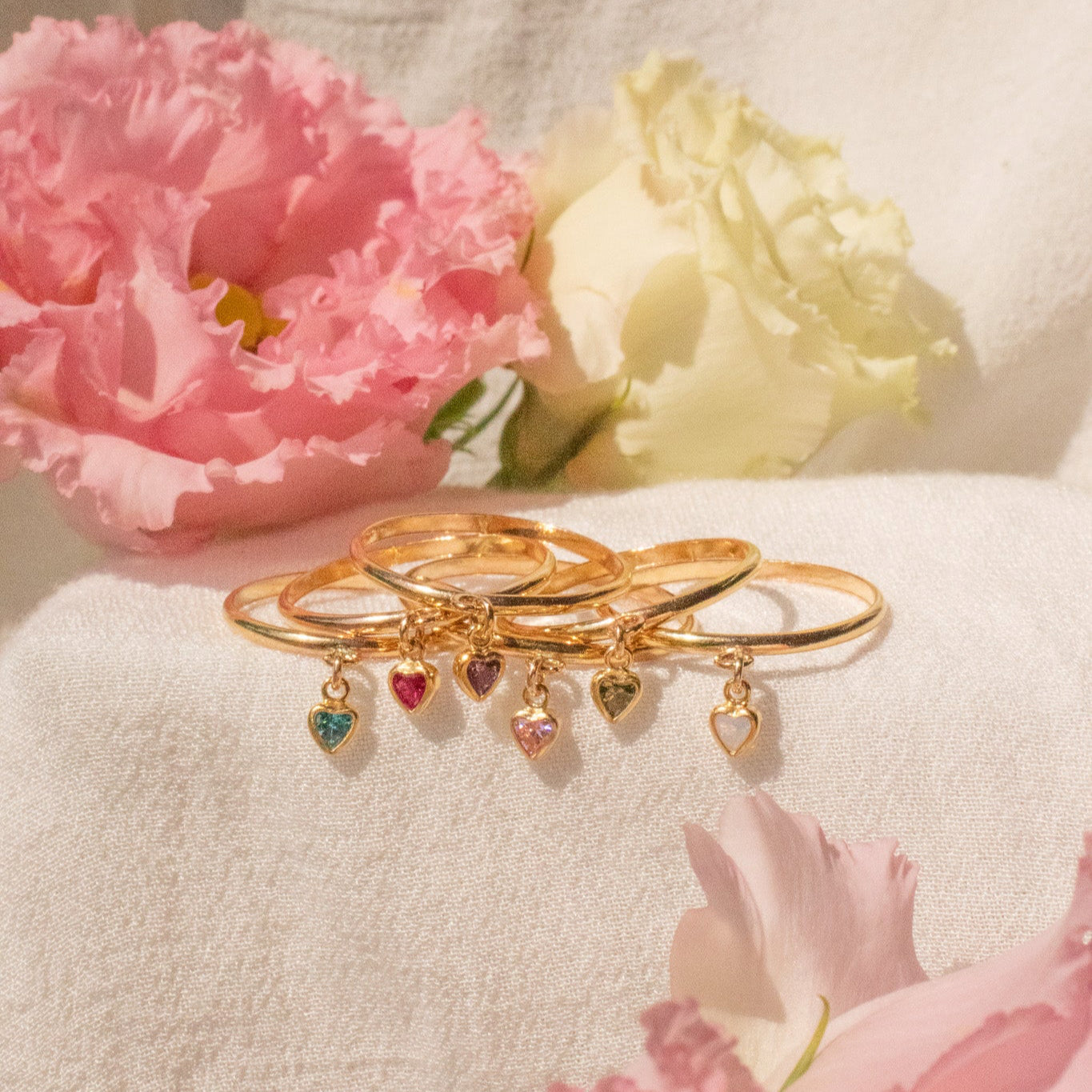 Gold rings with heart-shaped charms on a light background with pink flowers