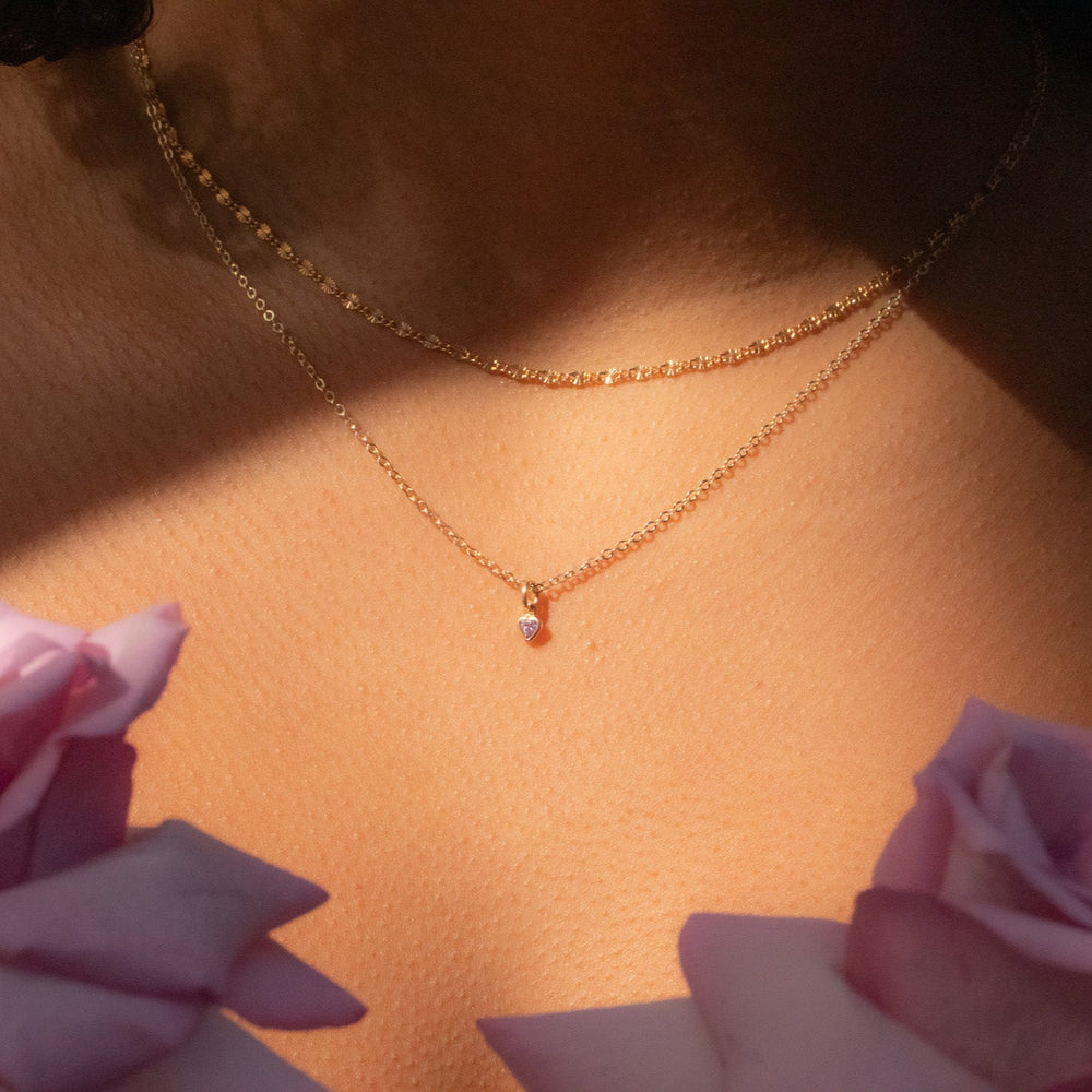 Close-up of a gold necklace with a small pendant, surrounded by pink roses.