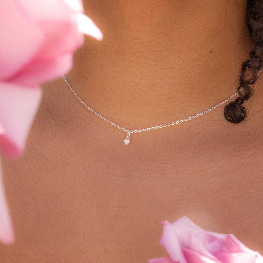 Necklace with a small pendant worn by a person with pink flowers in the background