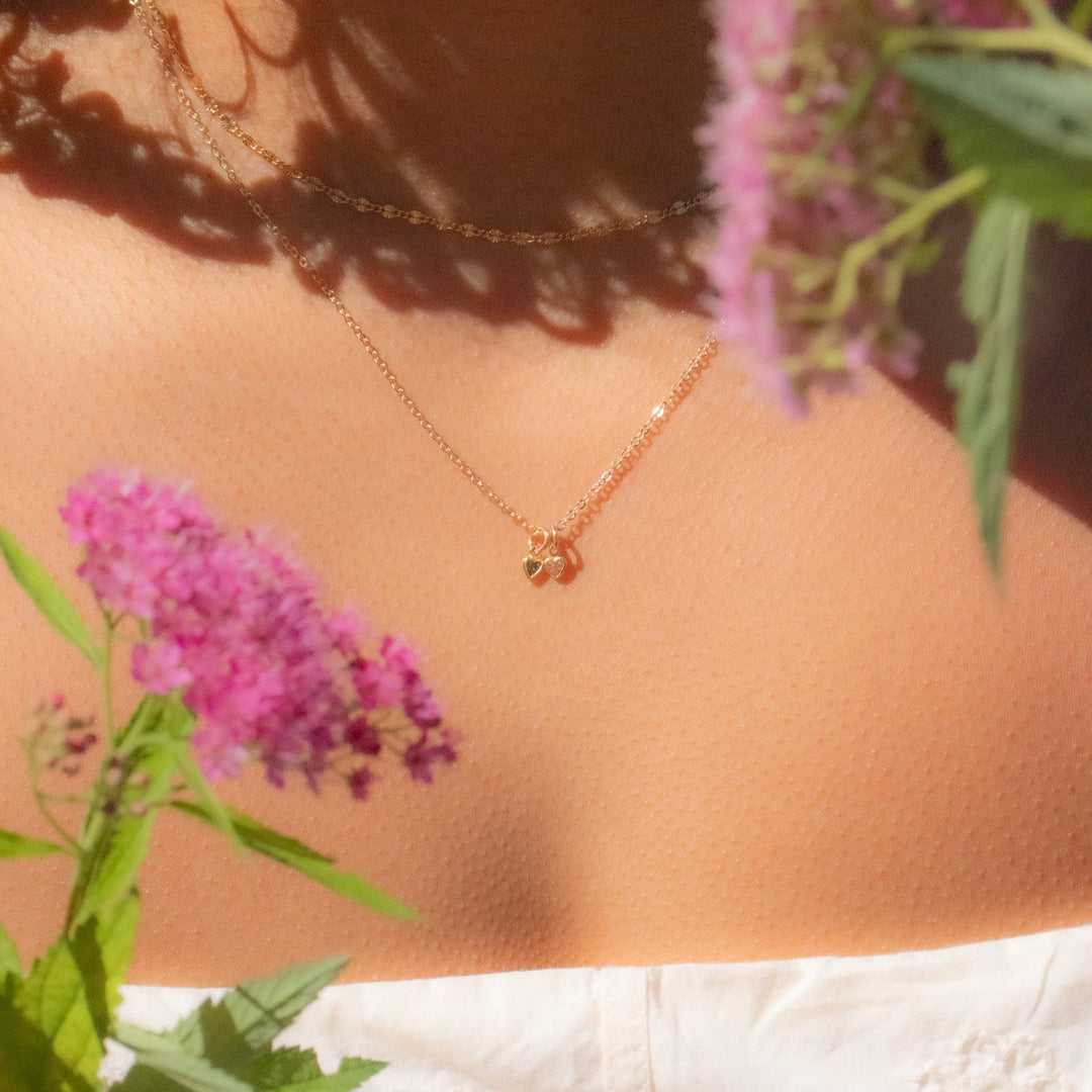 Person wearing a gold necklace with pink flowers and green leaves in the foreground