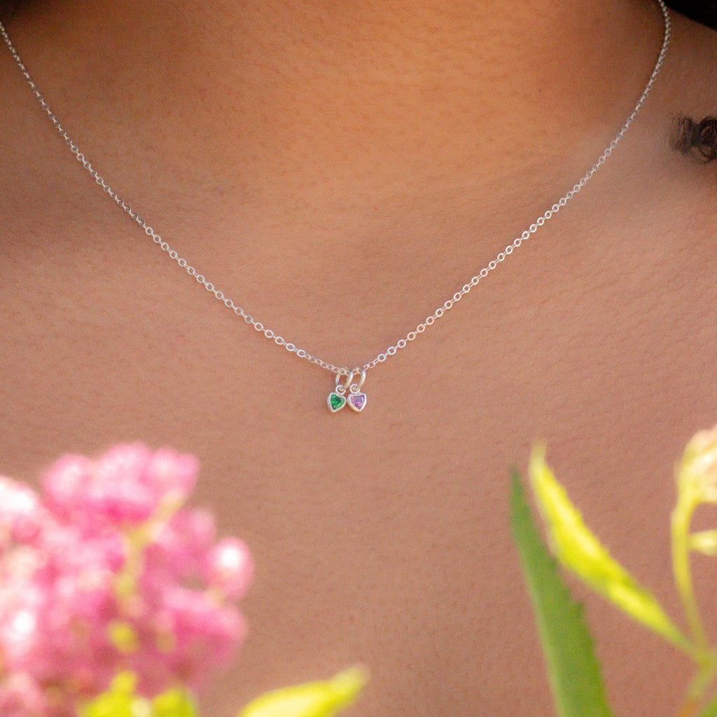 Silver necklace with small heart pendants on a blurred background with pink flowers and green leaves.