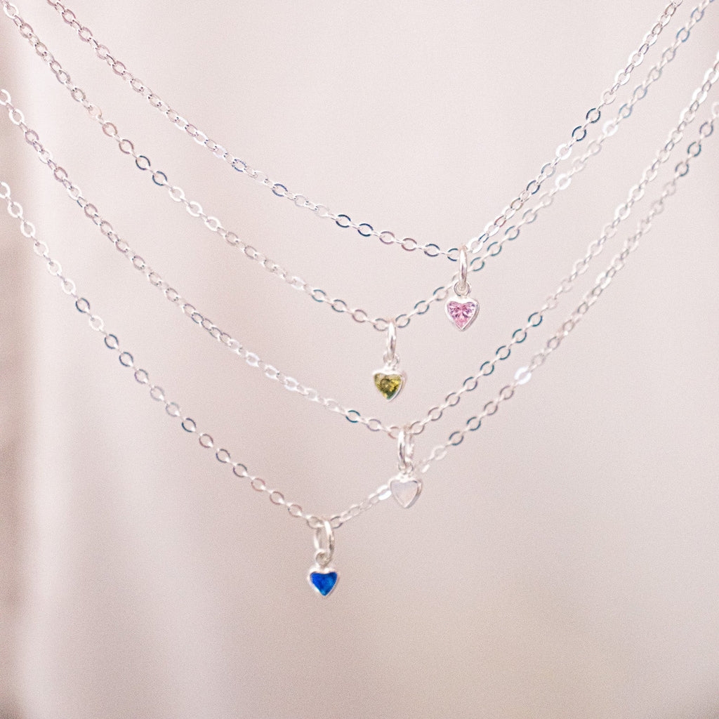 Stack of silver necklaces with heart-shaped charms on a light pink background