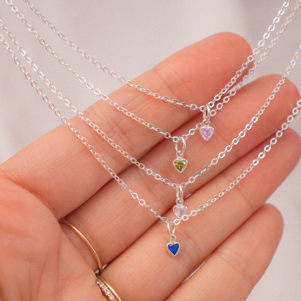  multiple silver necklaces with heart-shaped charms on a plain background