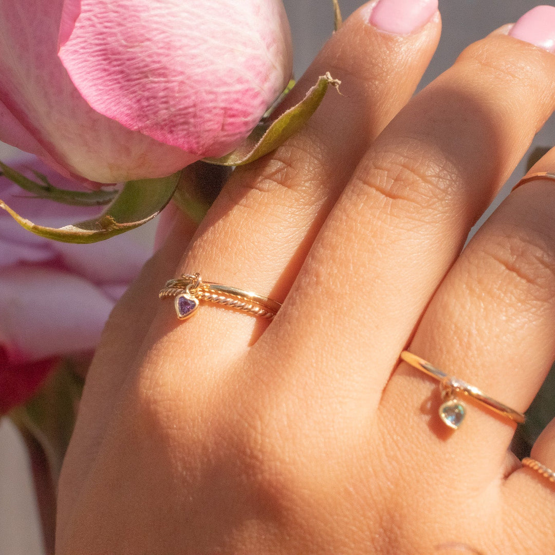 Hand wearing two gold rings with pink flowers in the background