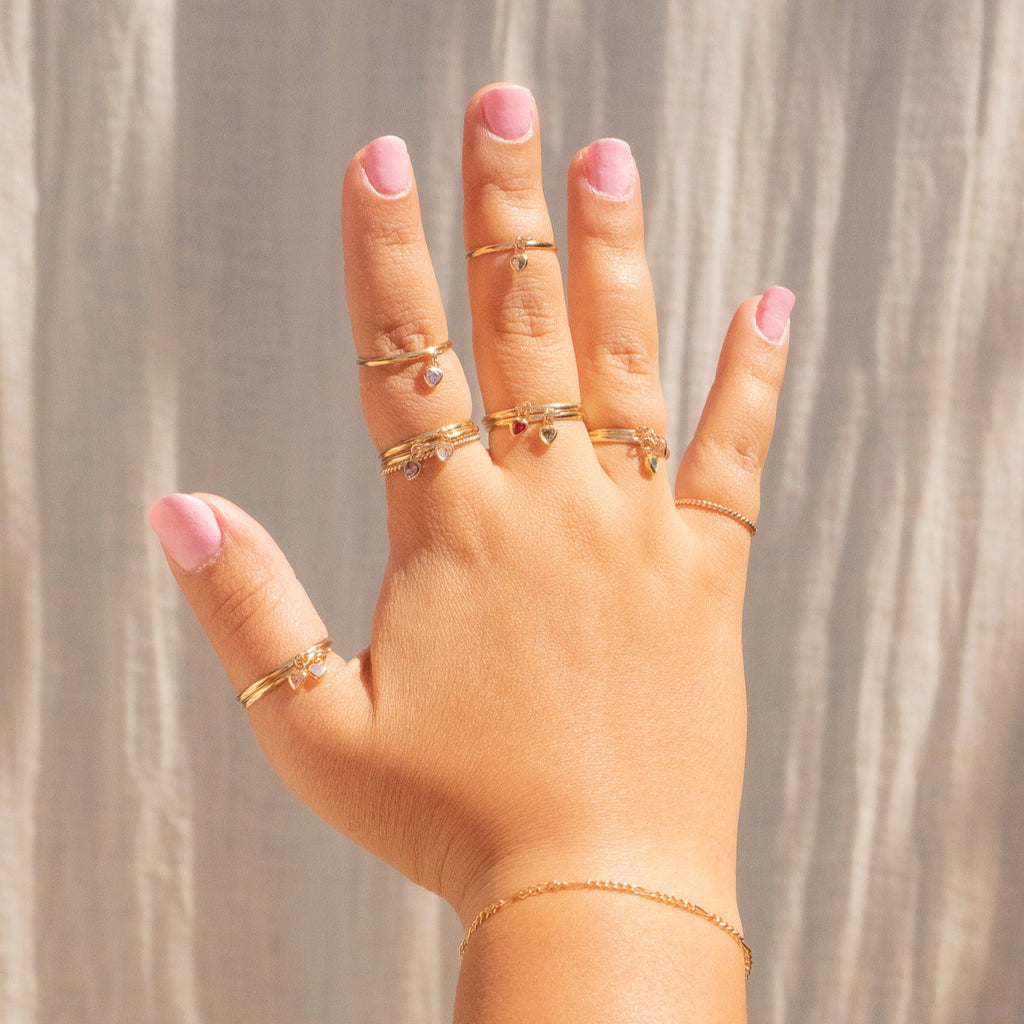 Hand wearing multiple gold rings with a neutral background