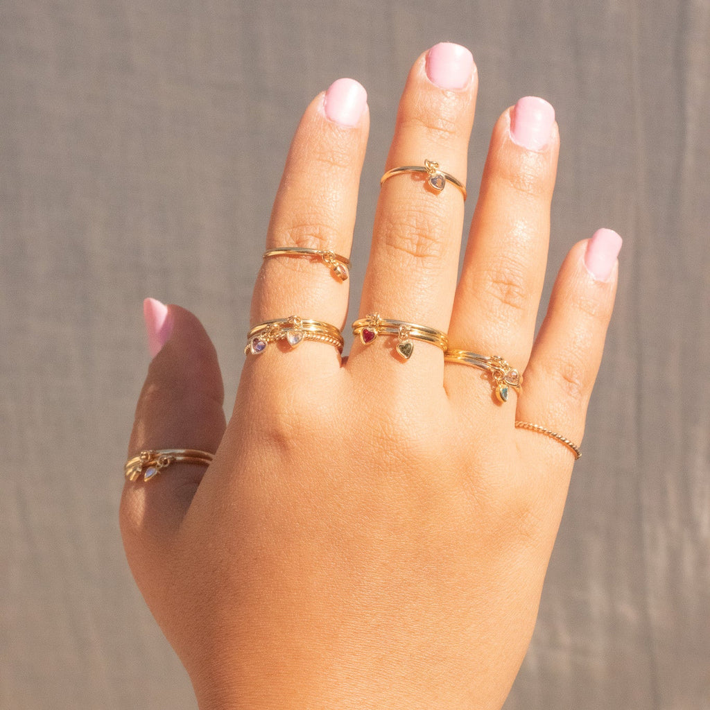 Hand wearing multiple gold rings on a neutral background