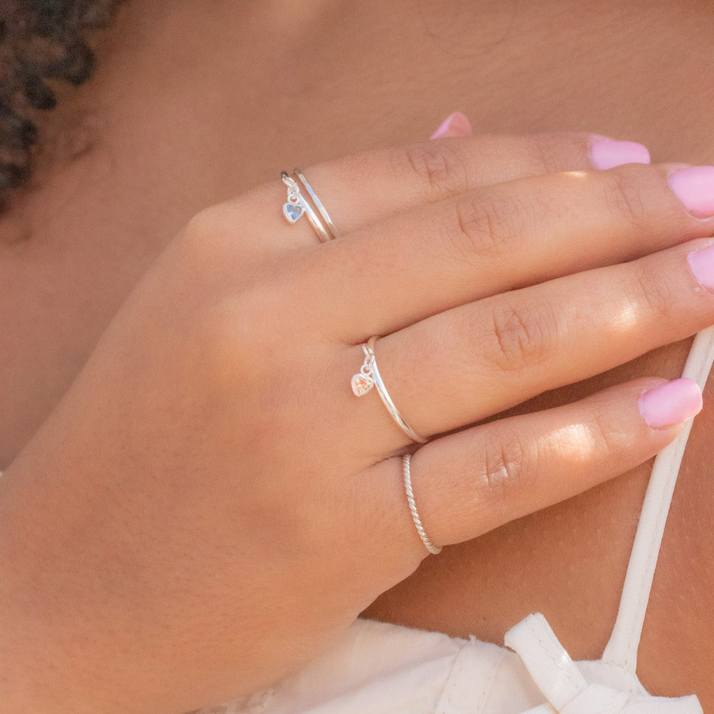 Close-up of a hand wearing multiple rings with pink nail polish on a blurred background
