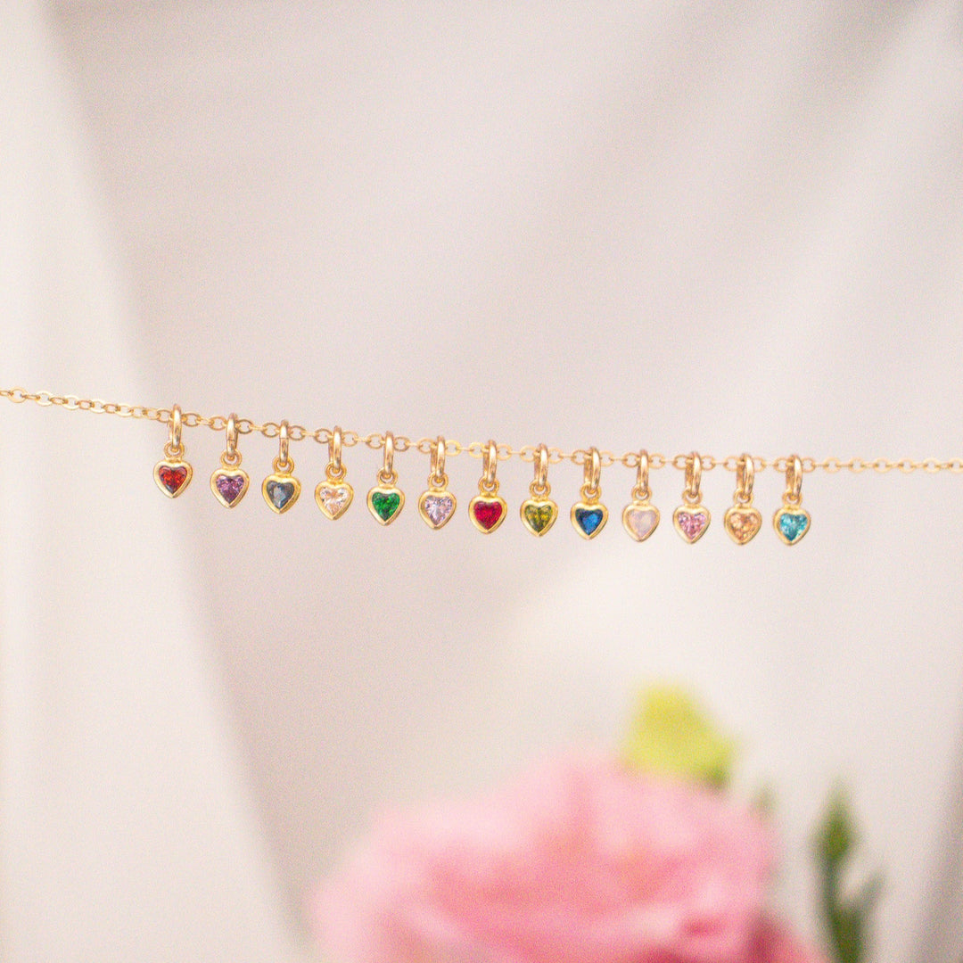 Gold necklace with heart-shaped colorful charms on a blurred floral background