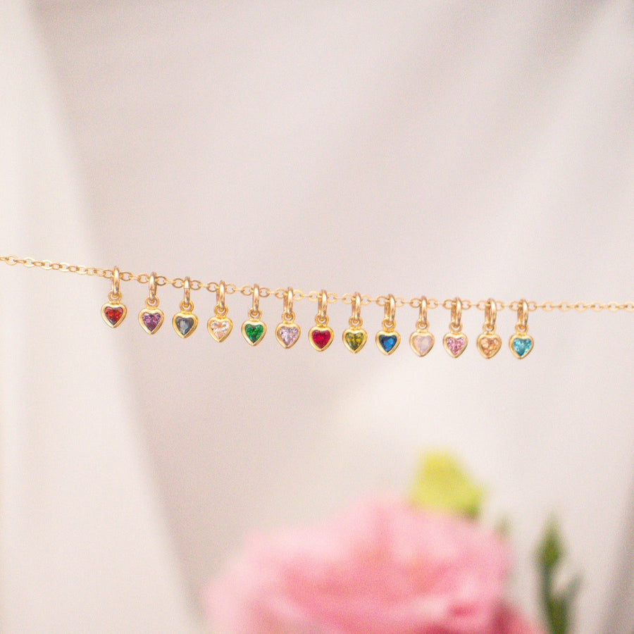 Gold necklace with heart-shaped colorful charms on a blurred floral background