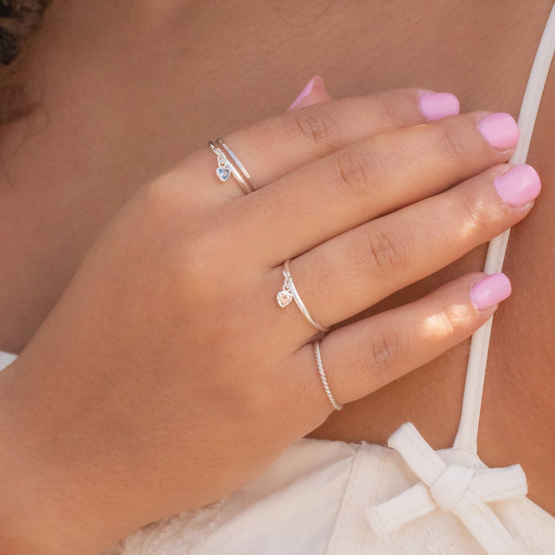 Close-up of a hand with pink nail polish wearing two silver rings on a blurred background
